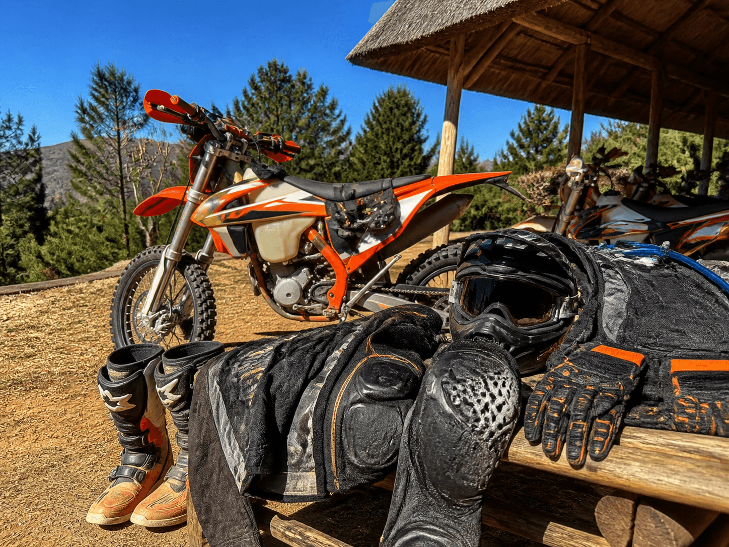 Enduro helmet, goggles, gloves, boots and protective kit beside an orange bike