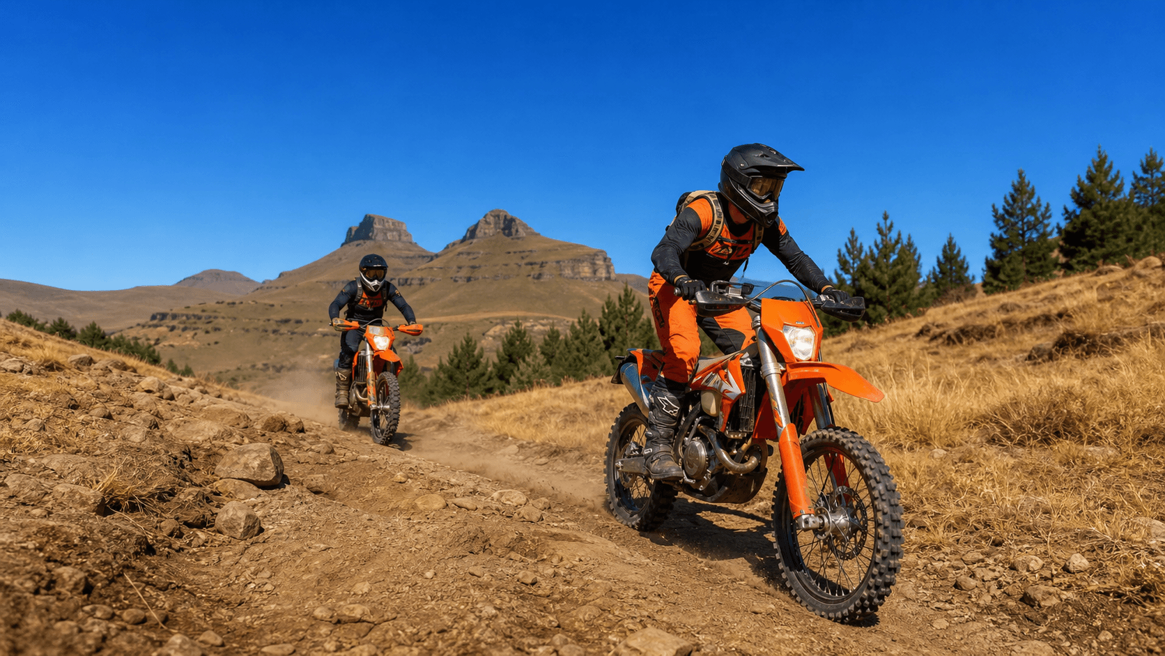 Two fully geared riders crossing a rocky mountain trail on orange enduro bikes