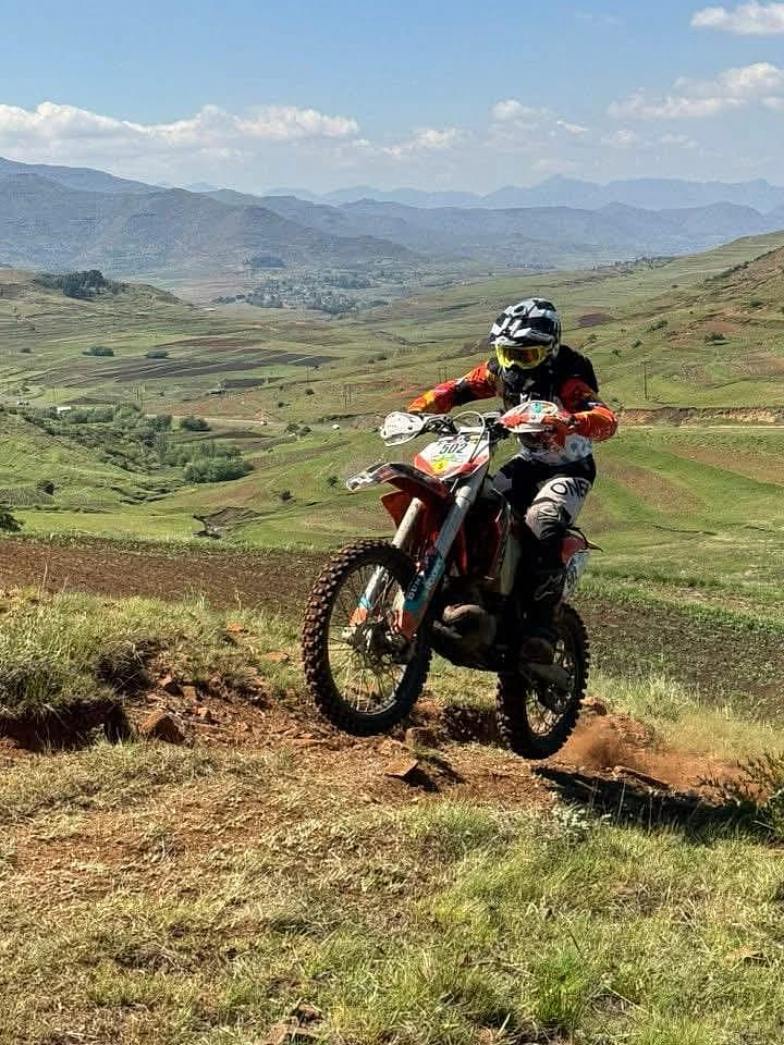 Helmeted enduro rider crossing a mountain trail with a highland valley behind them